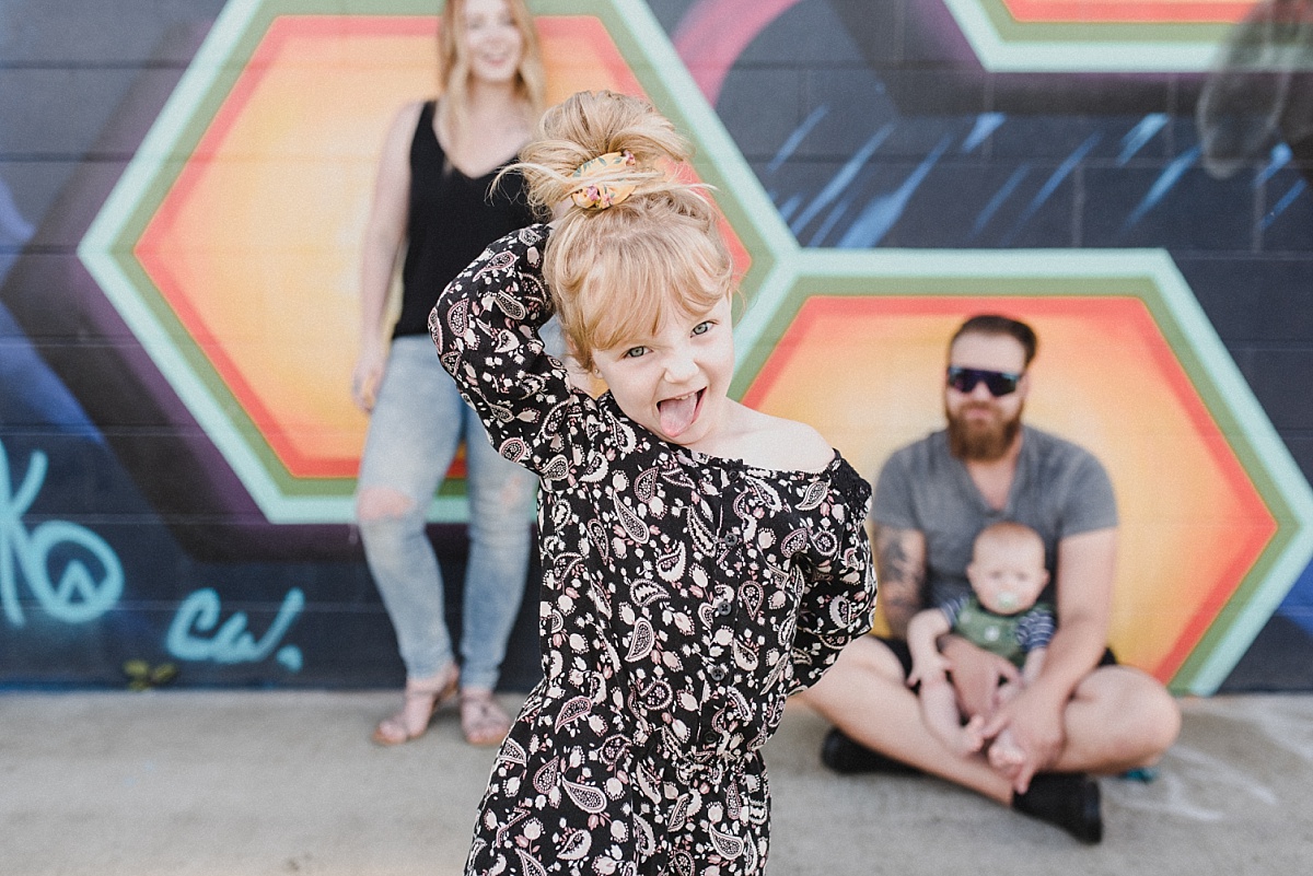 Cute, young girl makes a silly face at the camera as her family stands behind her