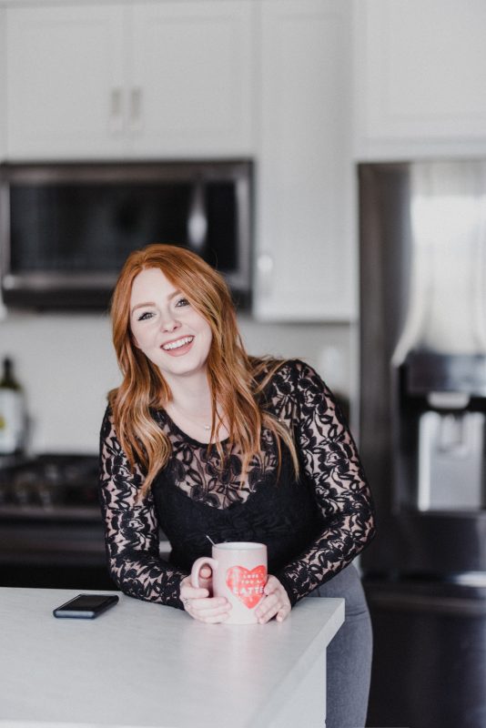 Kamloops Realtor Skyleigh McCallum smiles while holding a cup of coffee standing in her kitchen