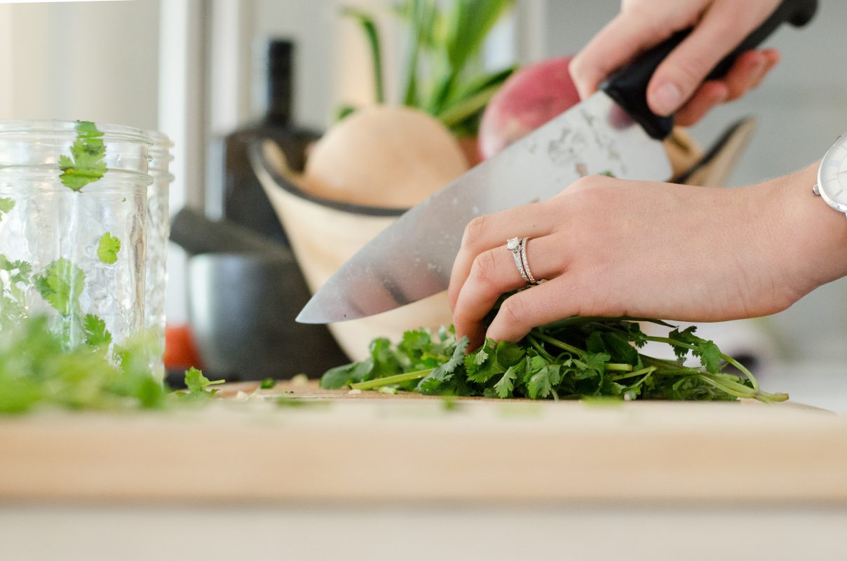 A woman's hands using a knife to cut herbs on a wood cutting board