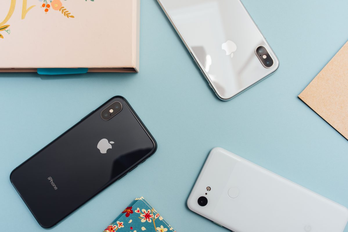 Three iphones laying on a blue table 