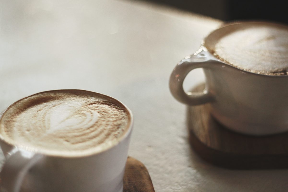 Two homemade lattes in ceramic cups sitting on wood coasters