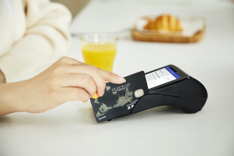 A woman's hand swiping a credit card after ordering an orange juice and a croissant.