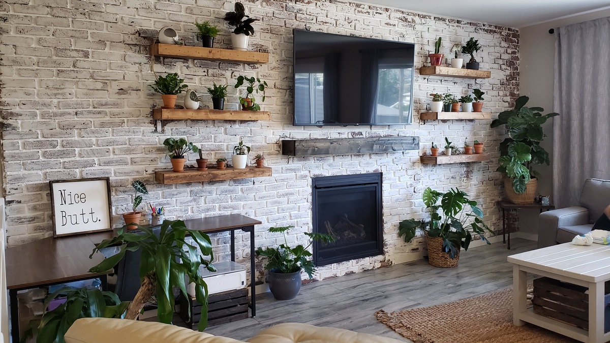A DIY faux brick wall diy home renovation project with brick tiles and german smear whitewash built around a fireplace and floating shelves.