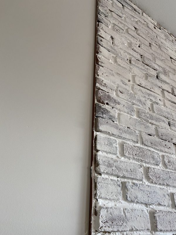 The edge of a faux brick wall with whitewash mortar where it meets the regular wall to show the brick wall edging.