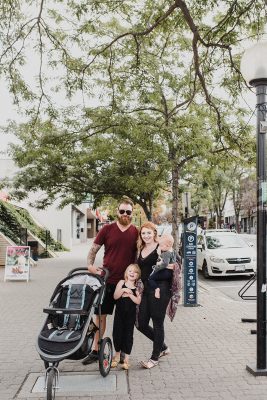 skyleigh mccallum kamloops realtor stands with her husband, baby son and four-year-old daughter on Victoria Street in kamloops in teh summer sunshine