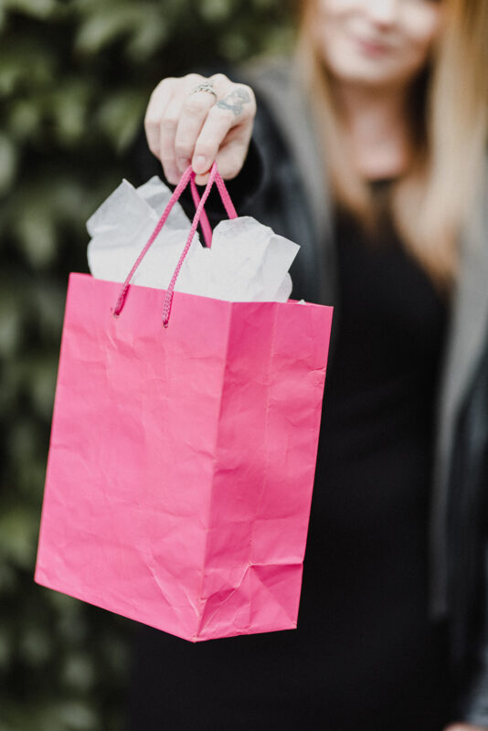 A Gen Z holding out a pink gift bag after shopping mindfully.