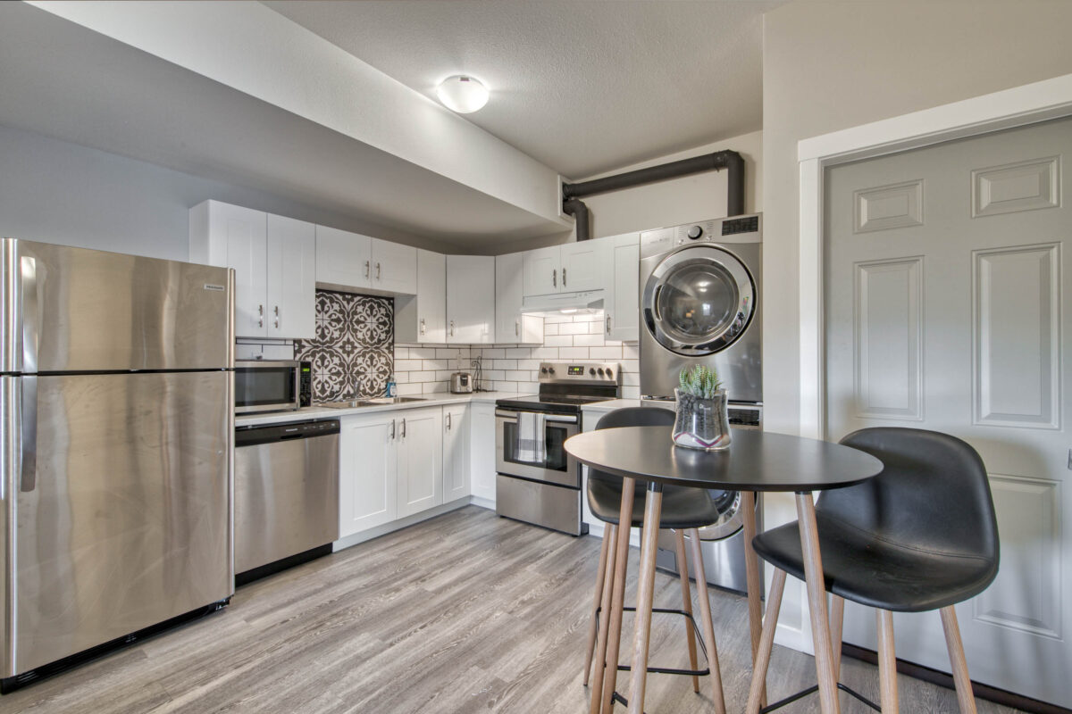 A modern kitchen with stainless steel appliances and stacked washer and dryer added by Airbnb hosts.