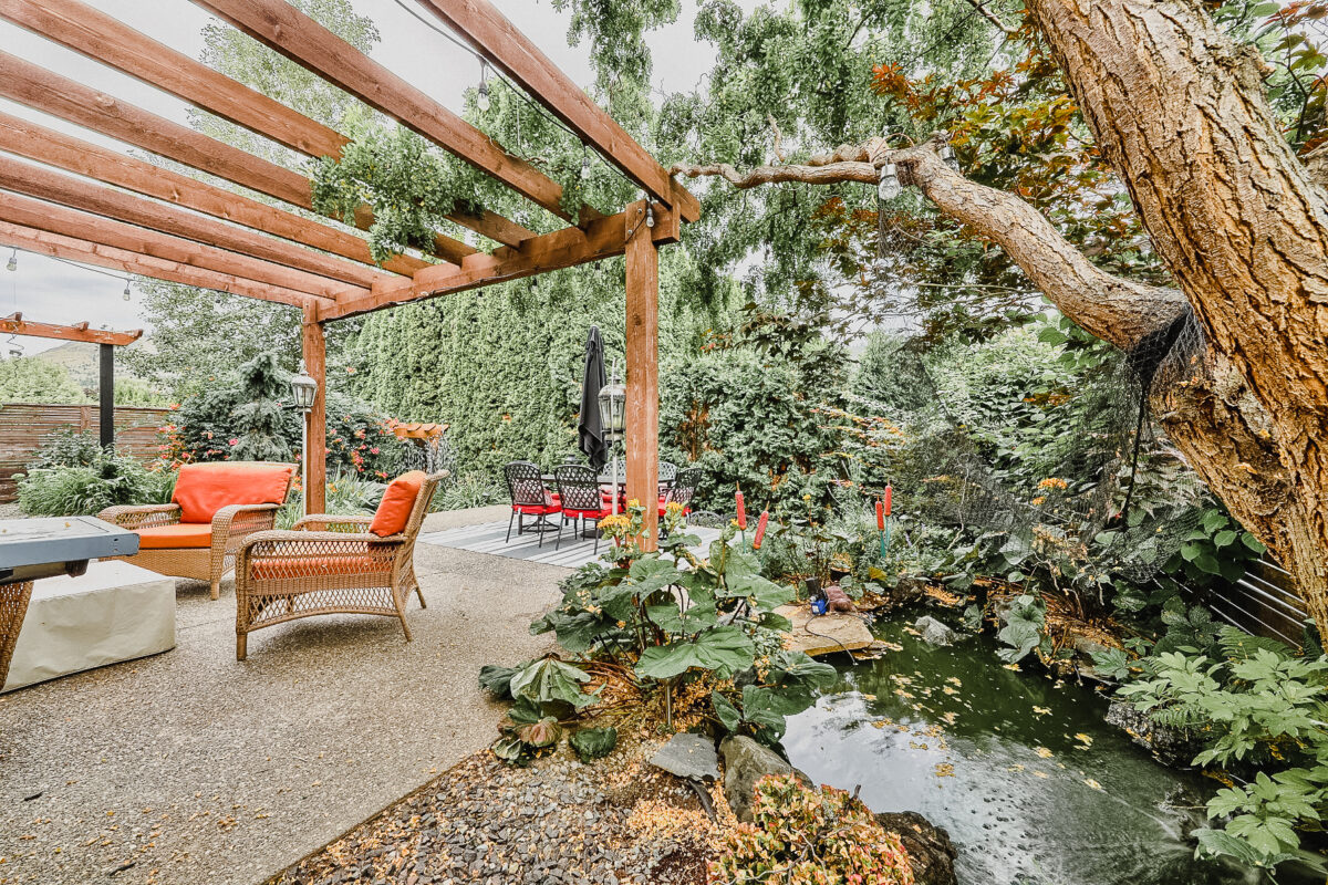 A beautiful, lush, green backyard of a home previously on the Kamloops real estate market with a pond, many plants and a sitting area.