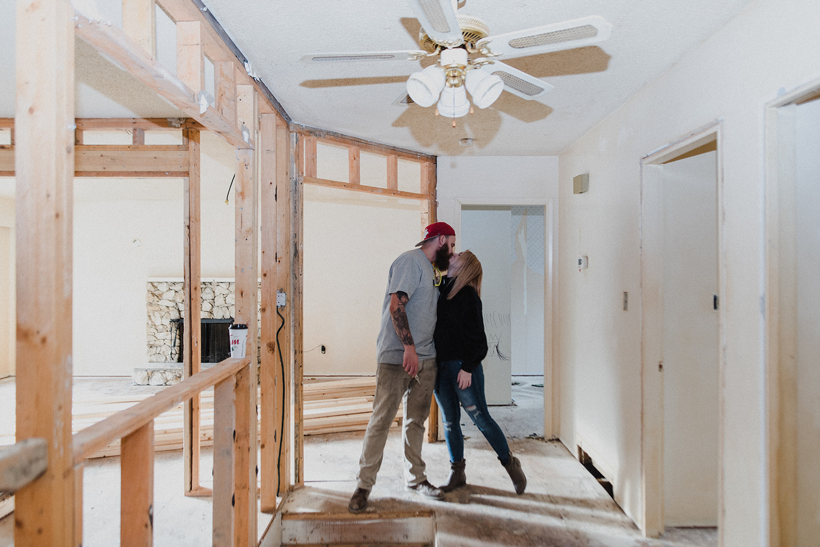 A man and woman kiss while standing in a house currently being renovated.
