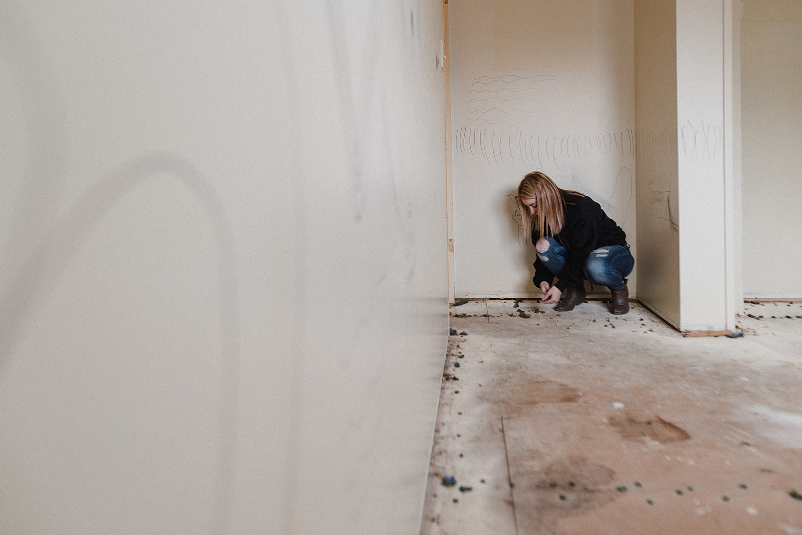 A woman wearing blue jeans and a black sweater kneels to work on renovations in a Kamloops home.