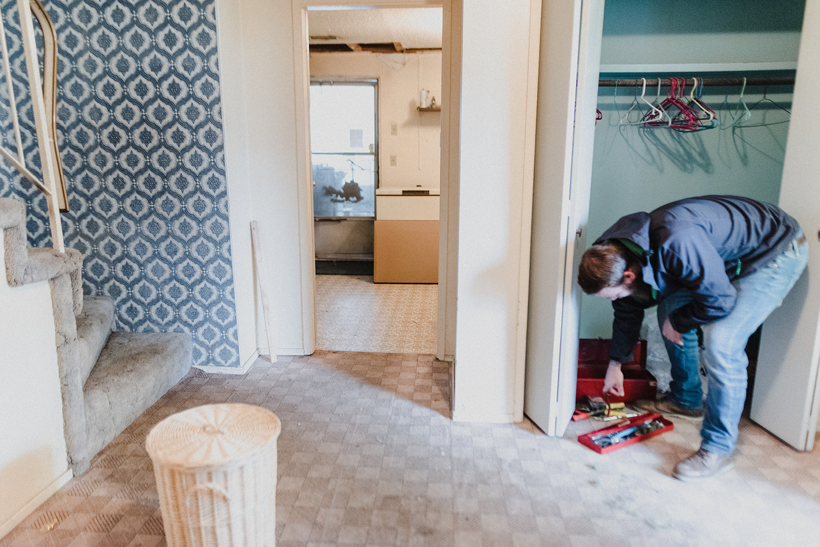 A man bends over to grab tools while working on renovating the home he's living in.