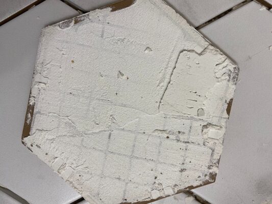 A white hexagon bathroom floor tile with mortar applied during a home renovation project.