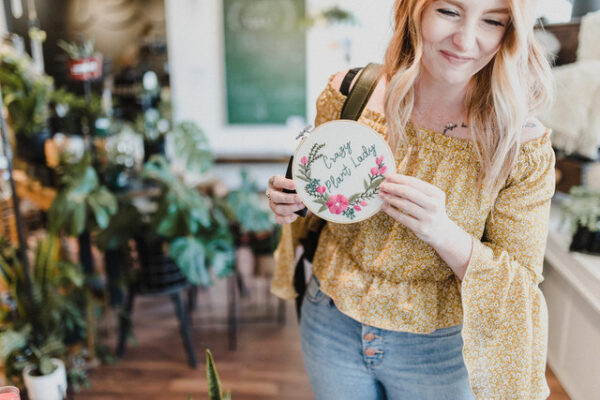 Kamloops Realtor Skyleigh McCallum holds a embroidered sign that says 'crazy plant lady' inside local store far and wide.