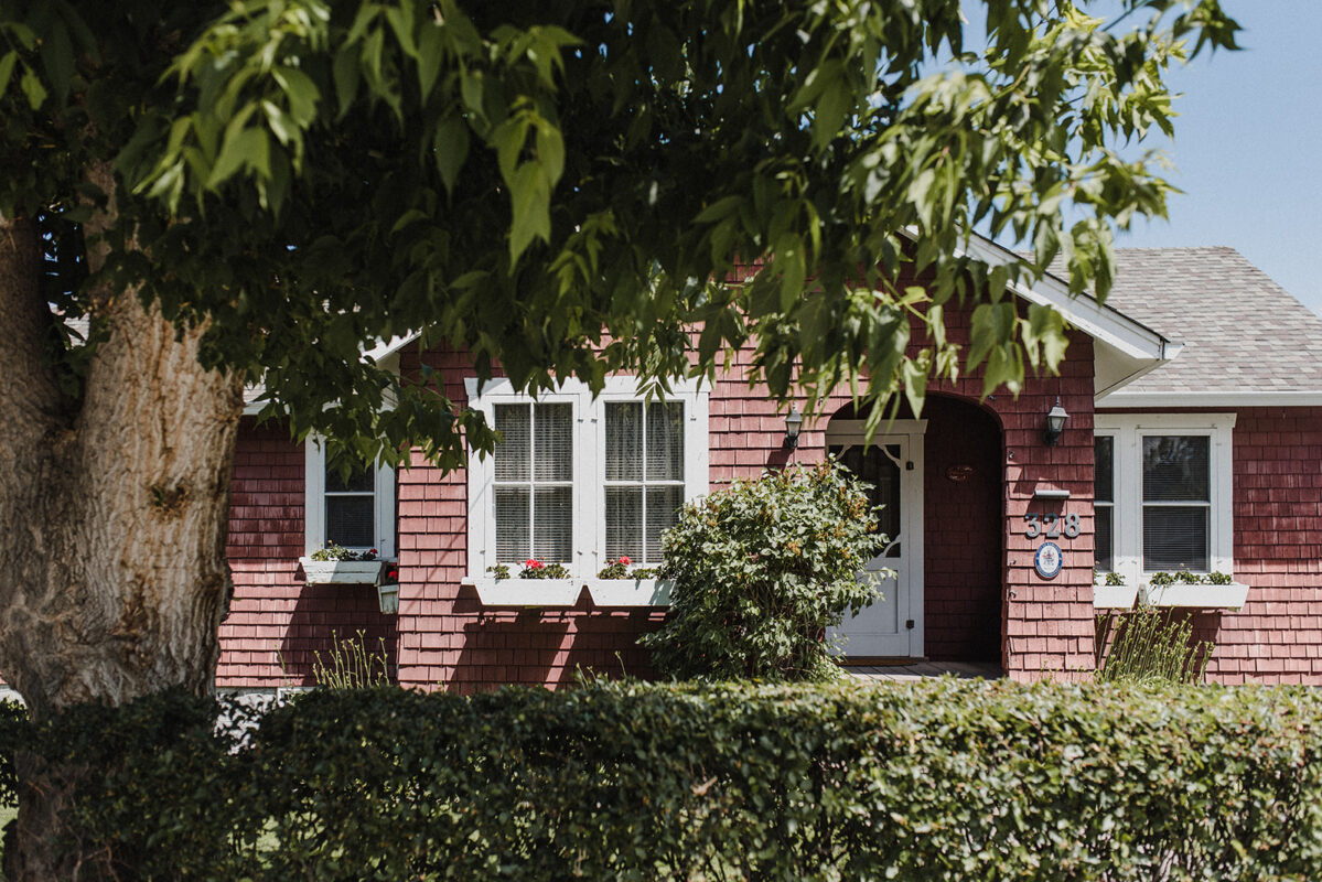 front door view of a cute red bungalow with a big tree out front